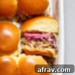 Pulled pork sliders in a dish with one turned on its side, ready to be eaten.
