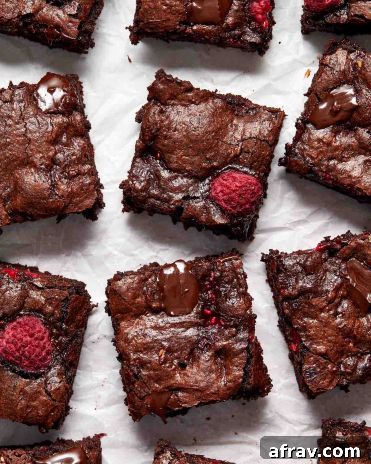 Brownies arranged on crinkled parchment paper, showcasing their fudgy texture and raspberry chunks.