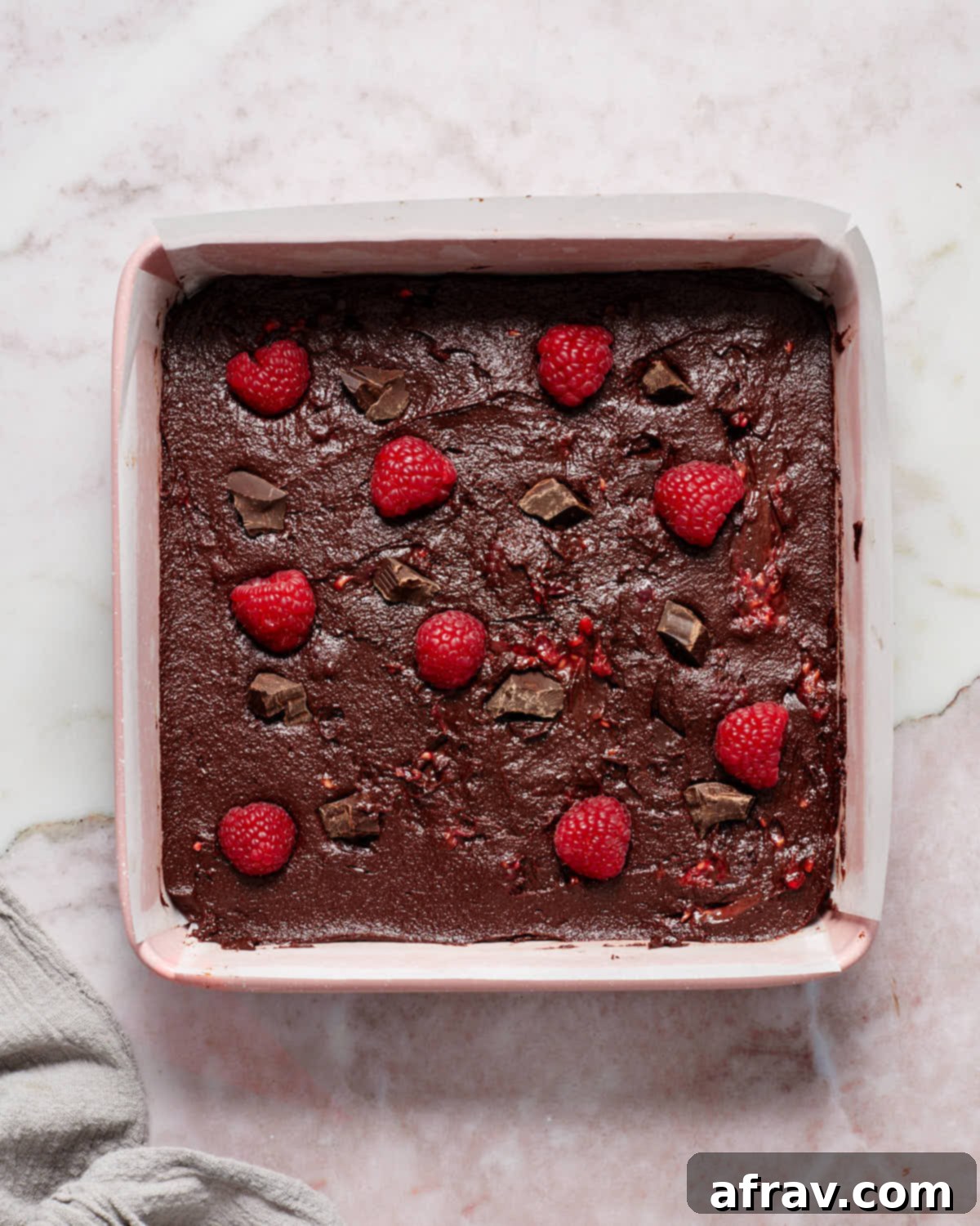 Batter spread out evenly in a square baking pan with fresh raspberries on top, ready to go into the oven.