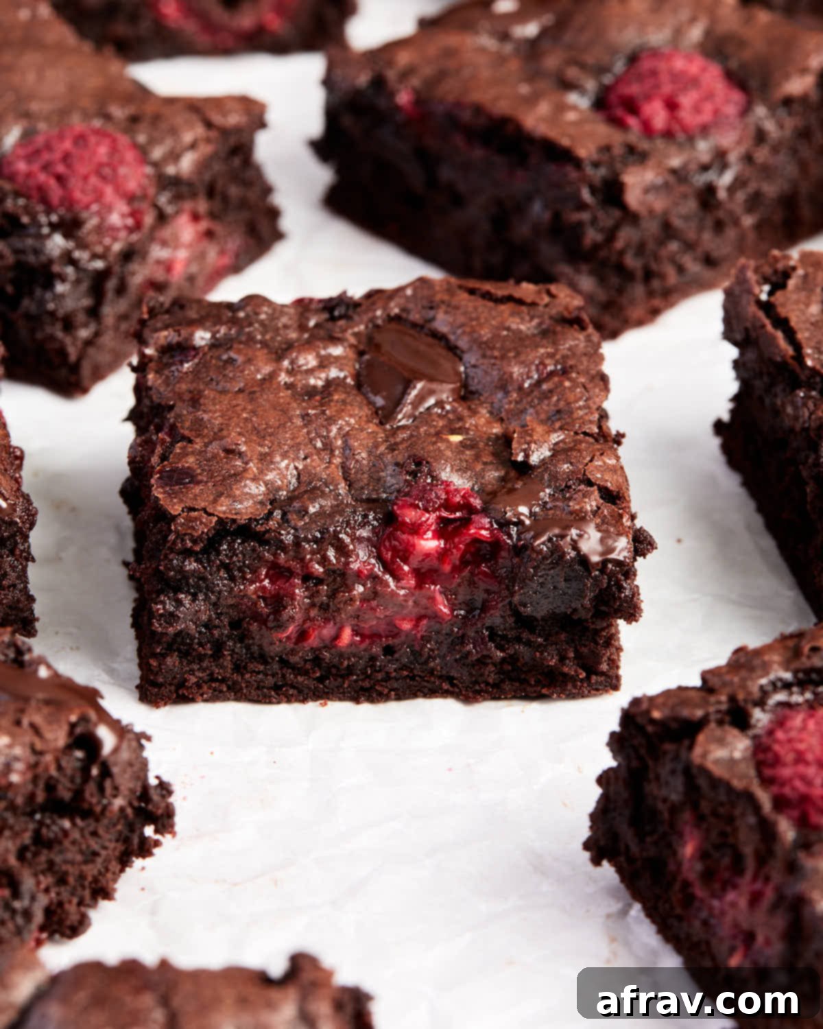 45-degree angle view of fudgy raspberry brownies arranged on white parchment paper, highlighting their perfect squares.