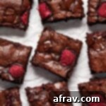 Raspberry brownies cut into squares and arranged on white parchment paper, highlighting their rich color and fruit inclusions.
