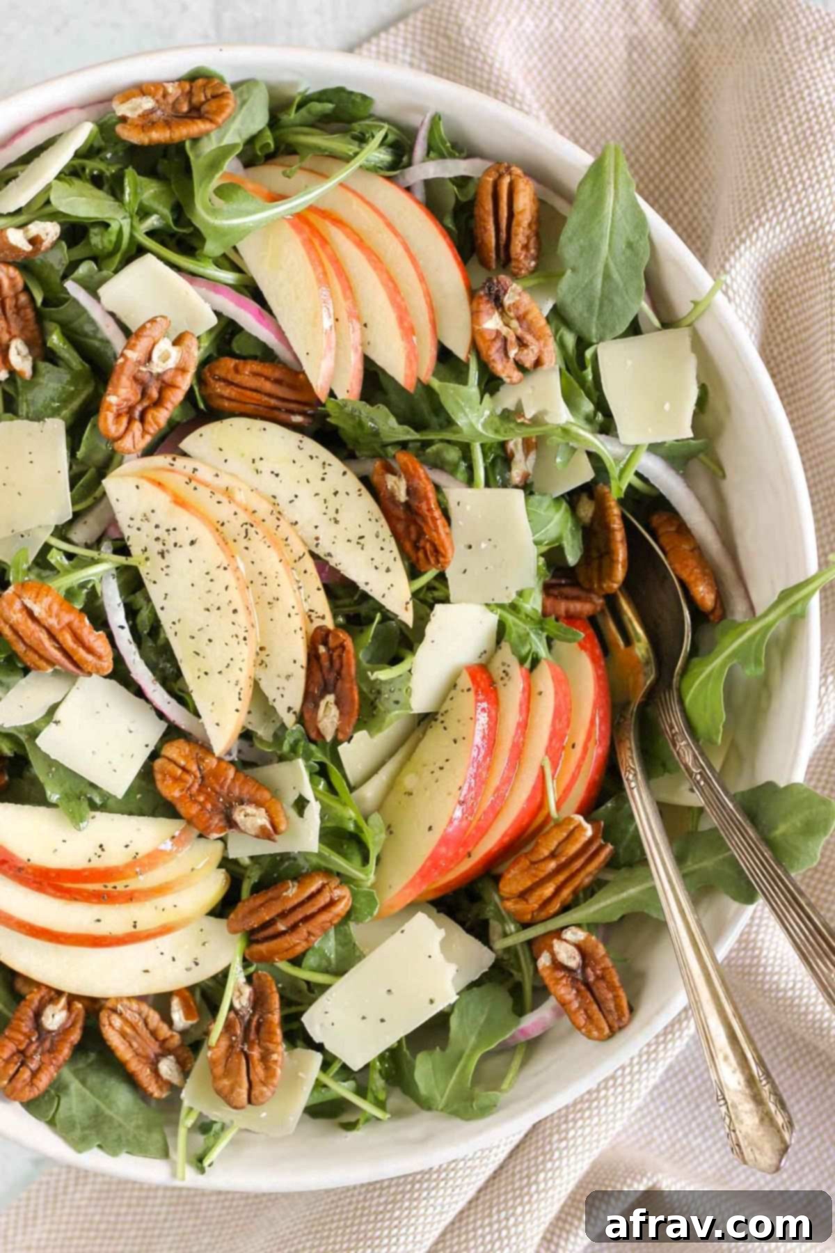 Arugula apple salad with pecans, parmesan cheese, and red onion in a large salad bowl with vintage utensils.