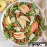 Arugula and apple salad with pecans, parmesan cheese, and red onion in a large salad bowl with vintage silverware.