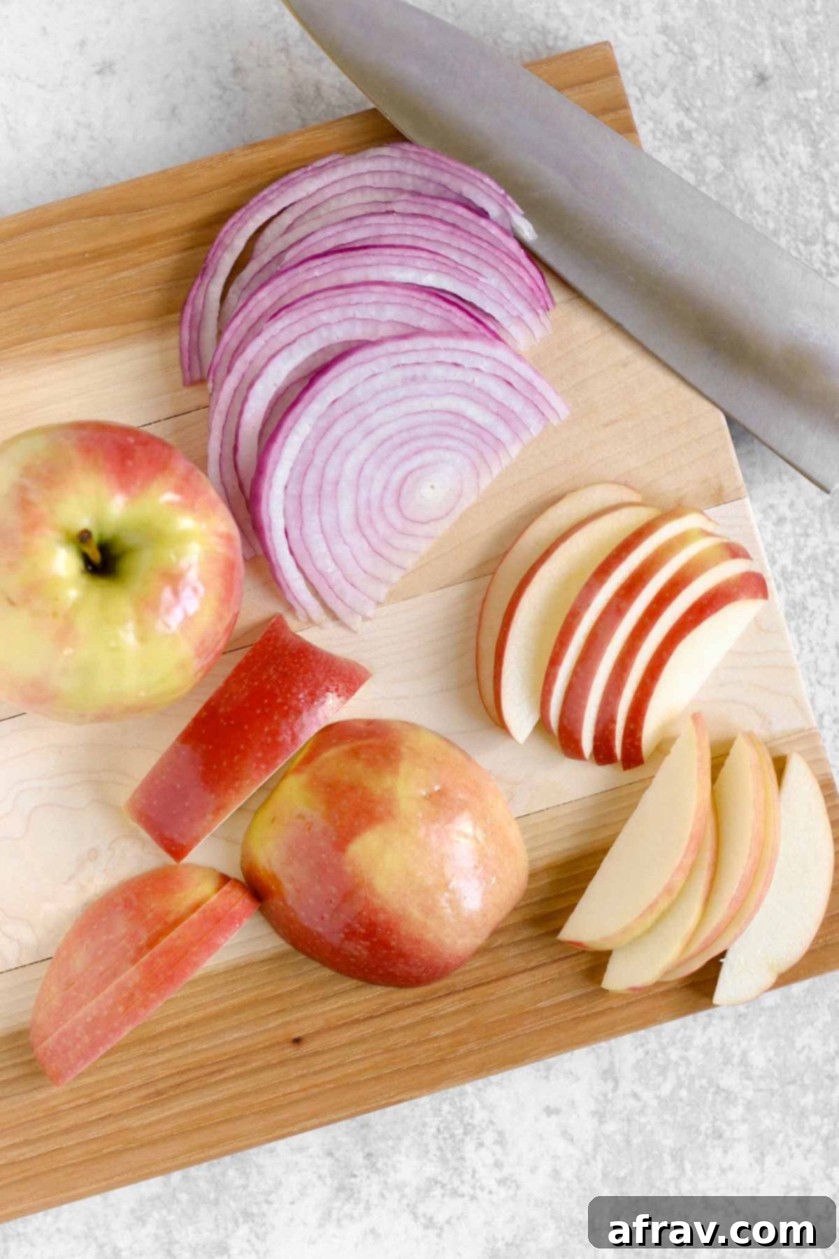 Sliced red onion and apples on a wood cutting board.
