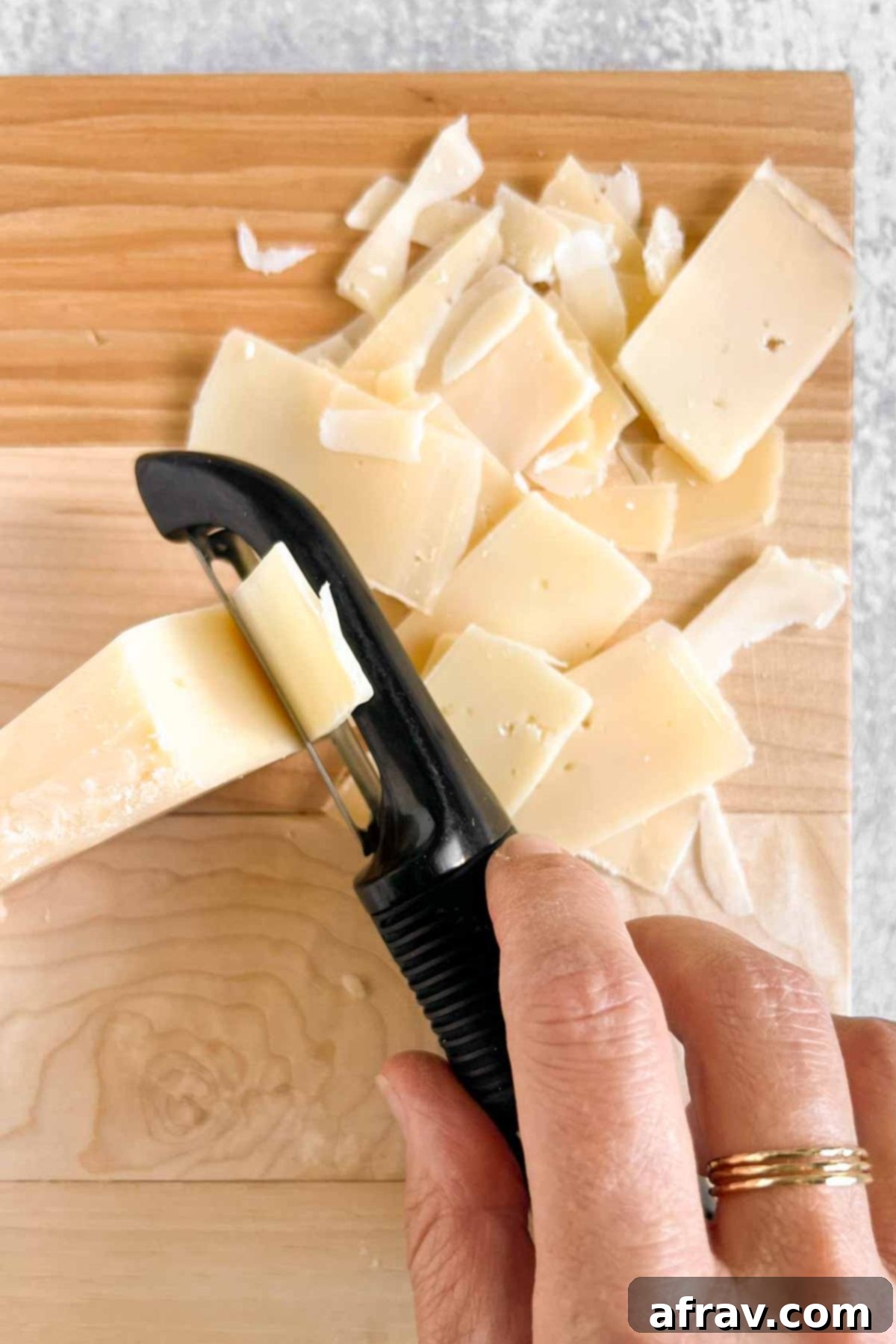 Vegetable peeler slicing a wedge of parmesan cheese.