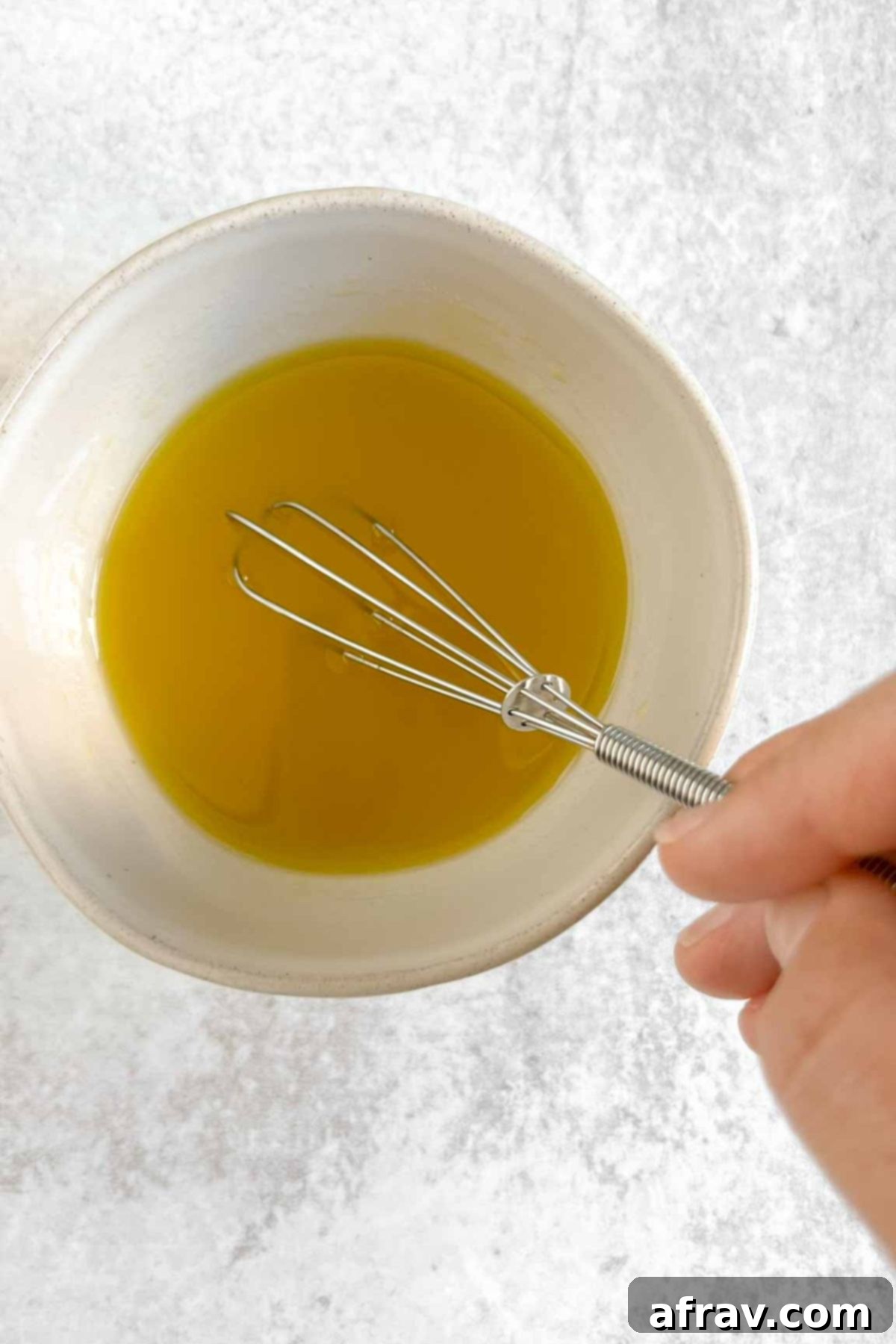 Small whisk whisking dressing ingredients in a small bowl.