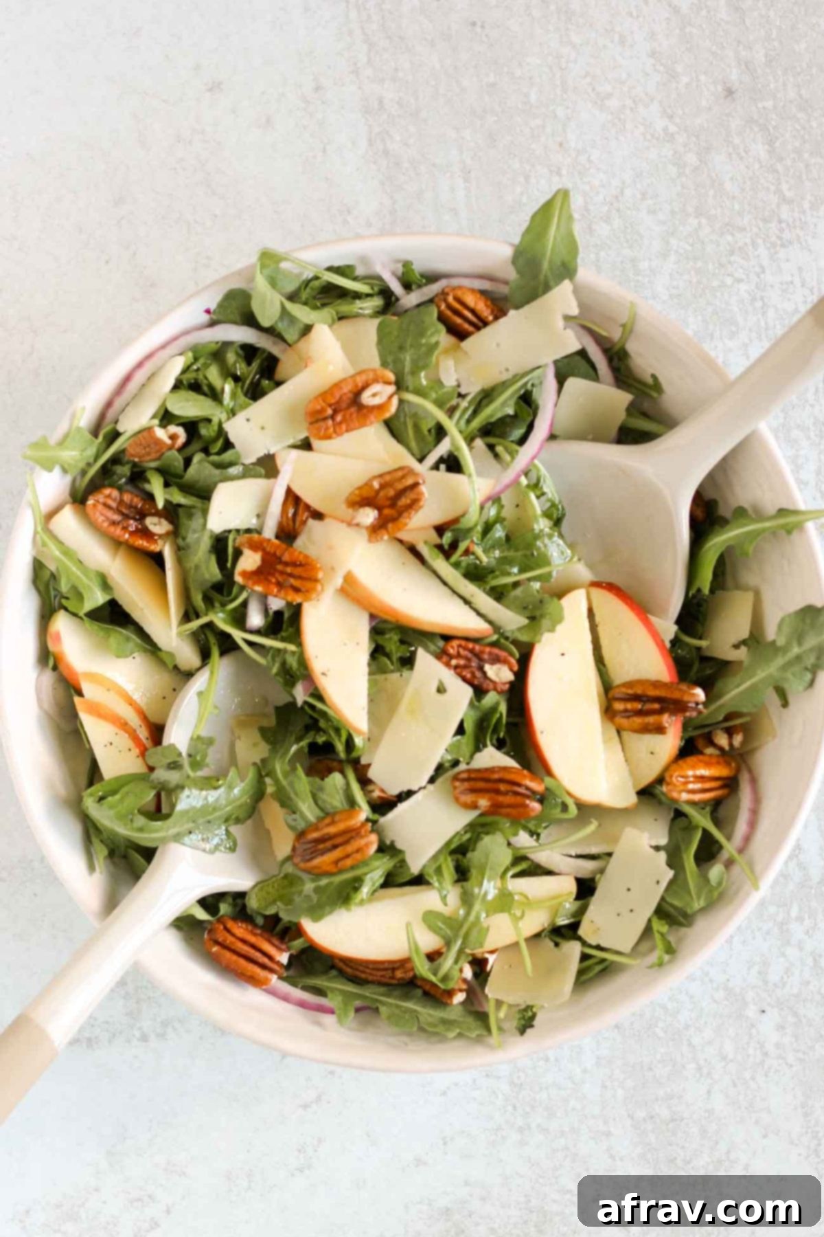 Arugula and apple salad being mixed together in a large salad bowl.