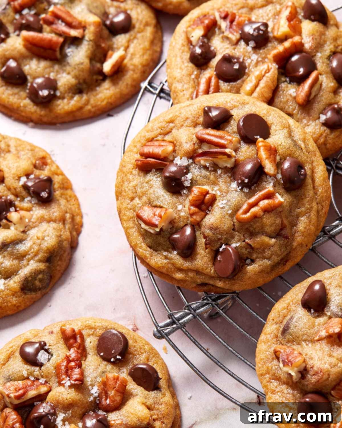 Close up of a cookie on a wire rack, showcasing its soft texture and visible chocolate and pecan pieces.