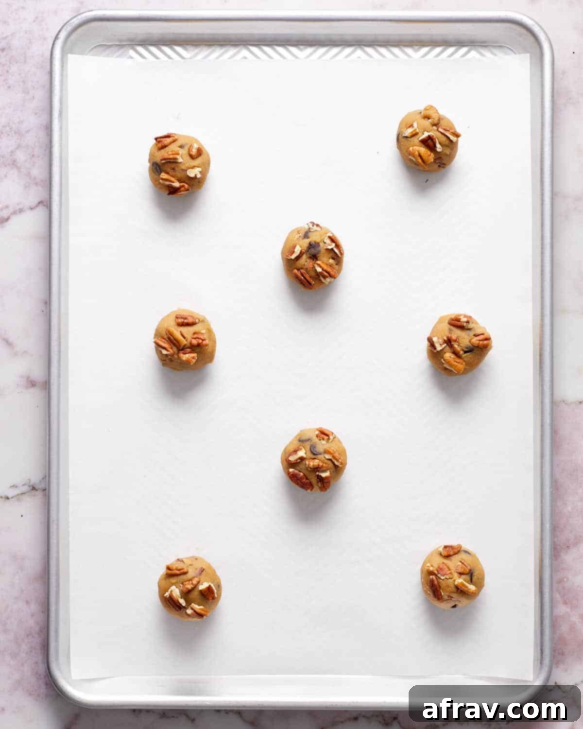 Cookie dough rolled into balls and arranged on a parchment paper lined baking sheet, topped with extra pecans.