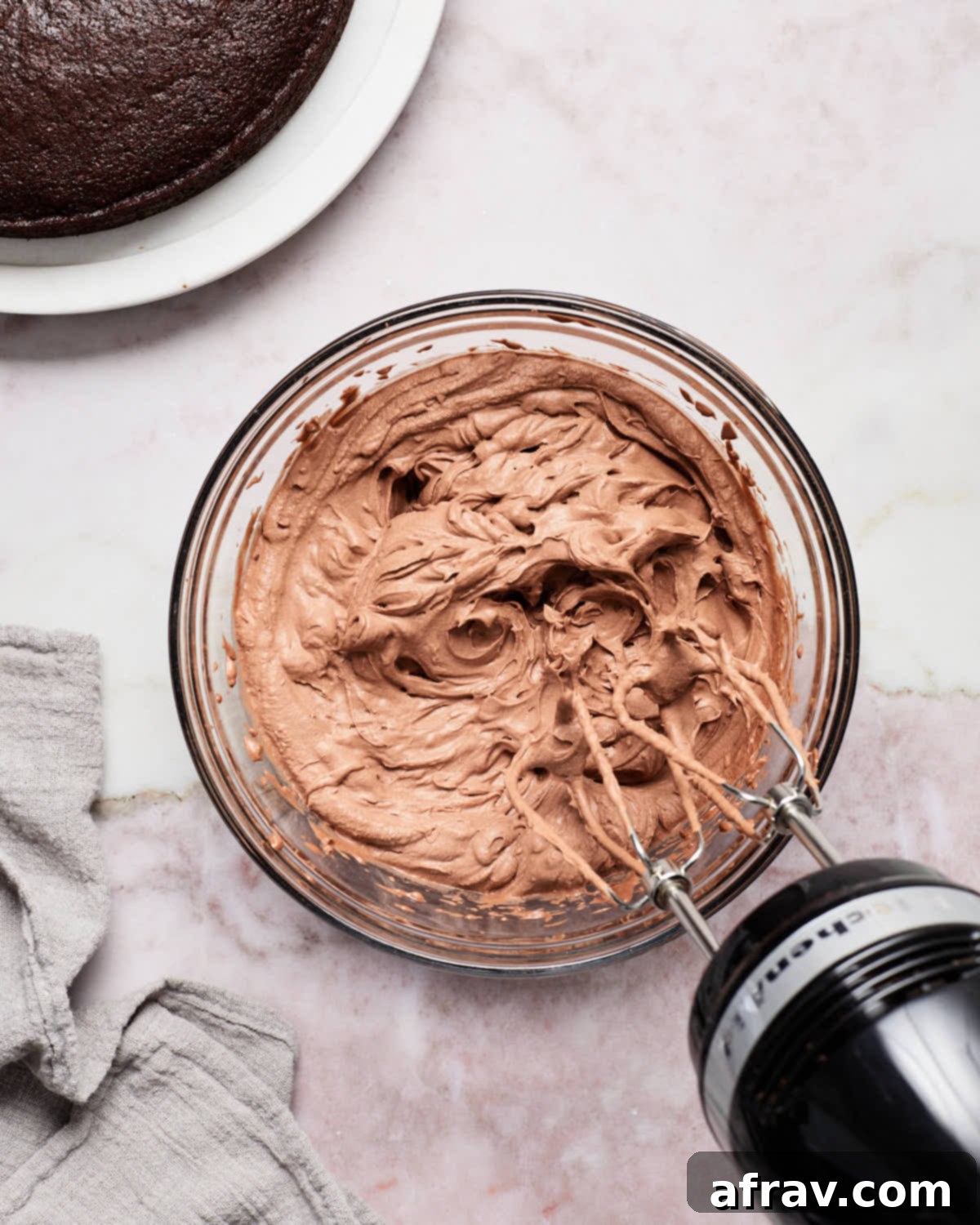 Dairy-free chocolate whipped cream frosting being vigorously whipped in a glass bowl with an electric mixer.