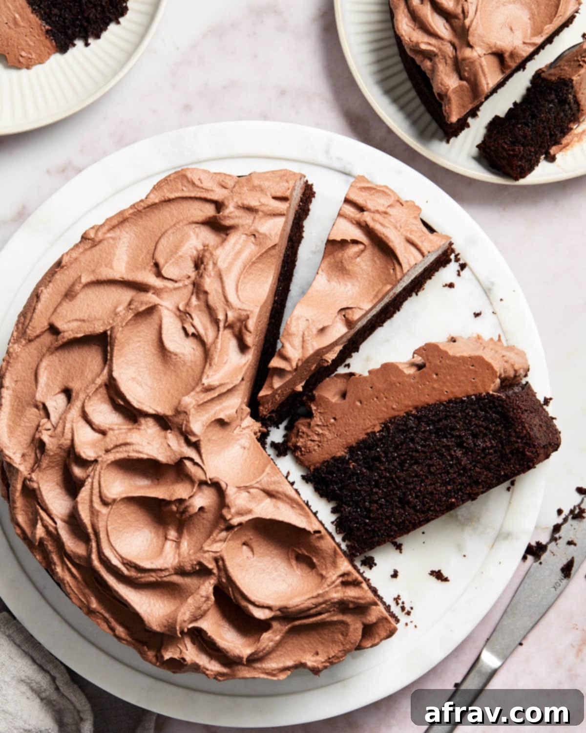 Overhead close-up view of the whole almond flour chocolate cake on a white cake plate, frosted and ready to serve.