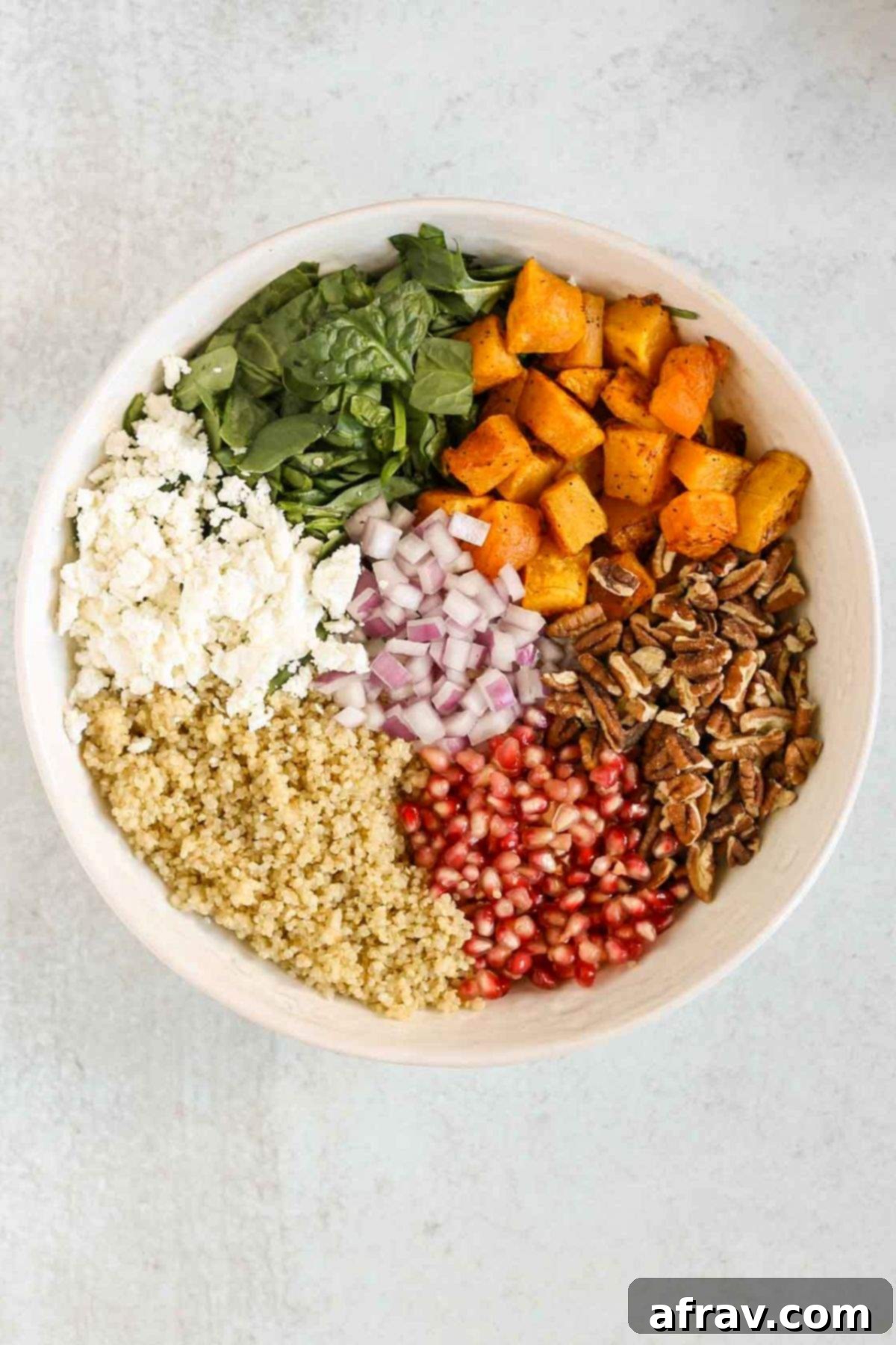 Harvest Quinoa Power Bowl 7 Butternut squash, pecans, pomegranate seeds, quinoa, goat cheese, spinach, and red onion all in separate piles in a large bowl.