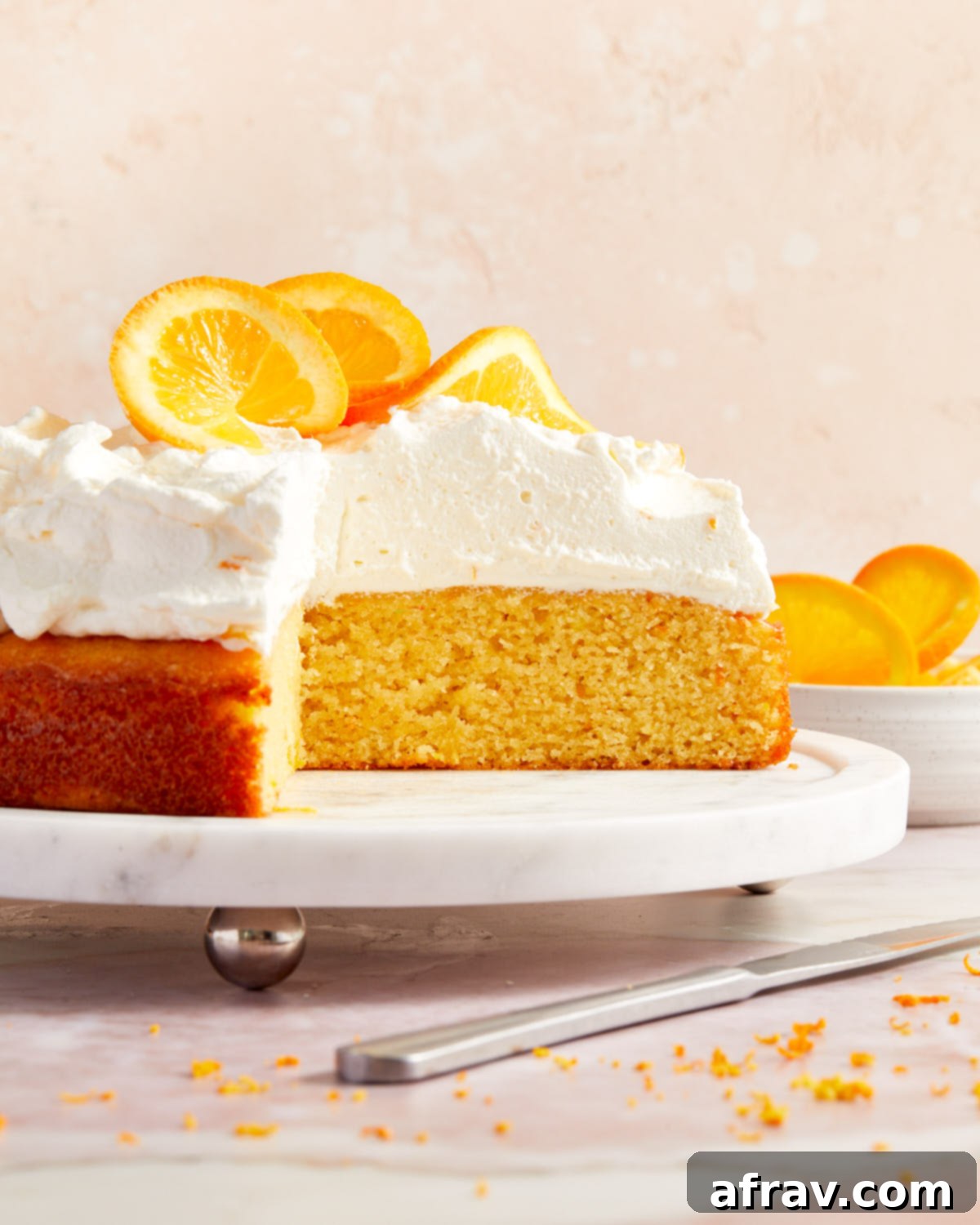 Orange Zest Almond Cake 2 Side view of orange almond flour cake on a white cake plate with slices of cake removed.