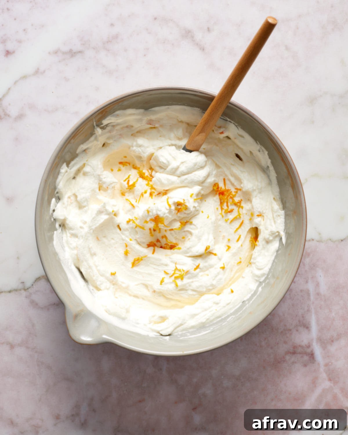 Orange Zest Almond Cake 6 Whipped cream topping in a grey bowl with a spatula stirring in orange zest.