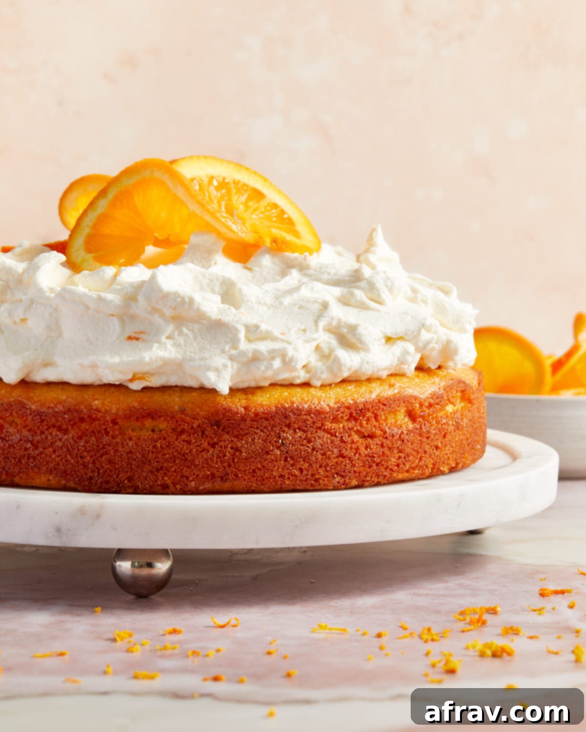Orange Zest Almond Cake 7 Side view of orange cake topped with whipped cream and orange slices on a white cake plate.