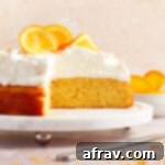 Orange Zest Almond Cake 10 Side view of almond flour orange cake on a white cake stand with whipped cream and oranges on top and some slices of cake removed.