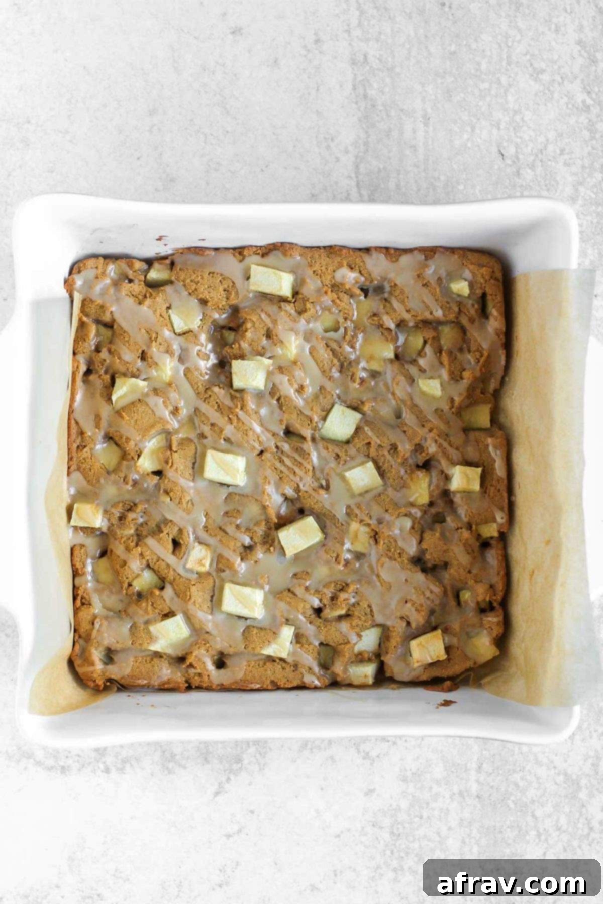 Uncut apple blondie bars with a generous drizzle of maple glaze in a square baking dish.