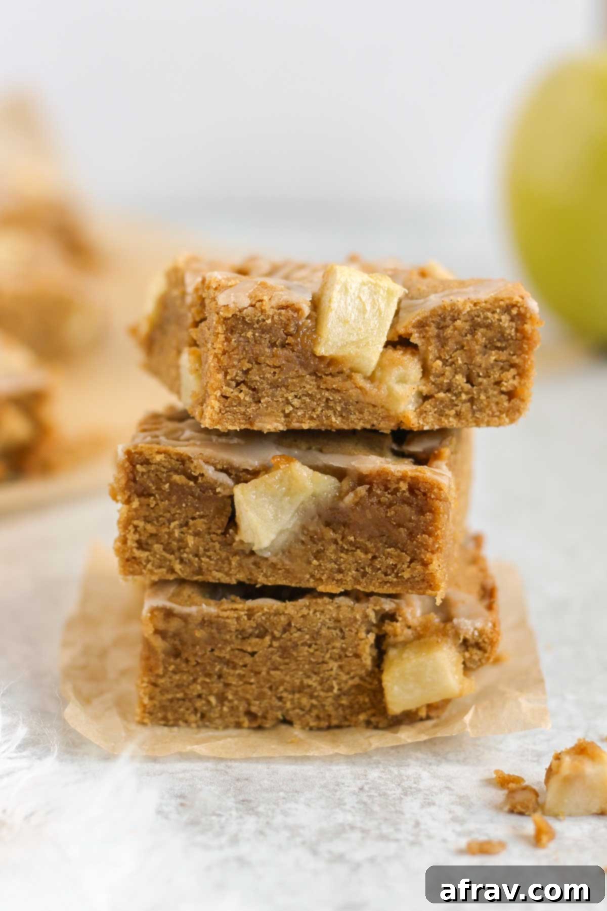 Three gluten-free apple blondie bars stacked high with a fresh green apple in the background.