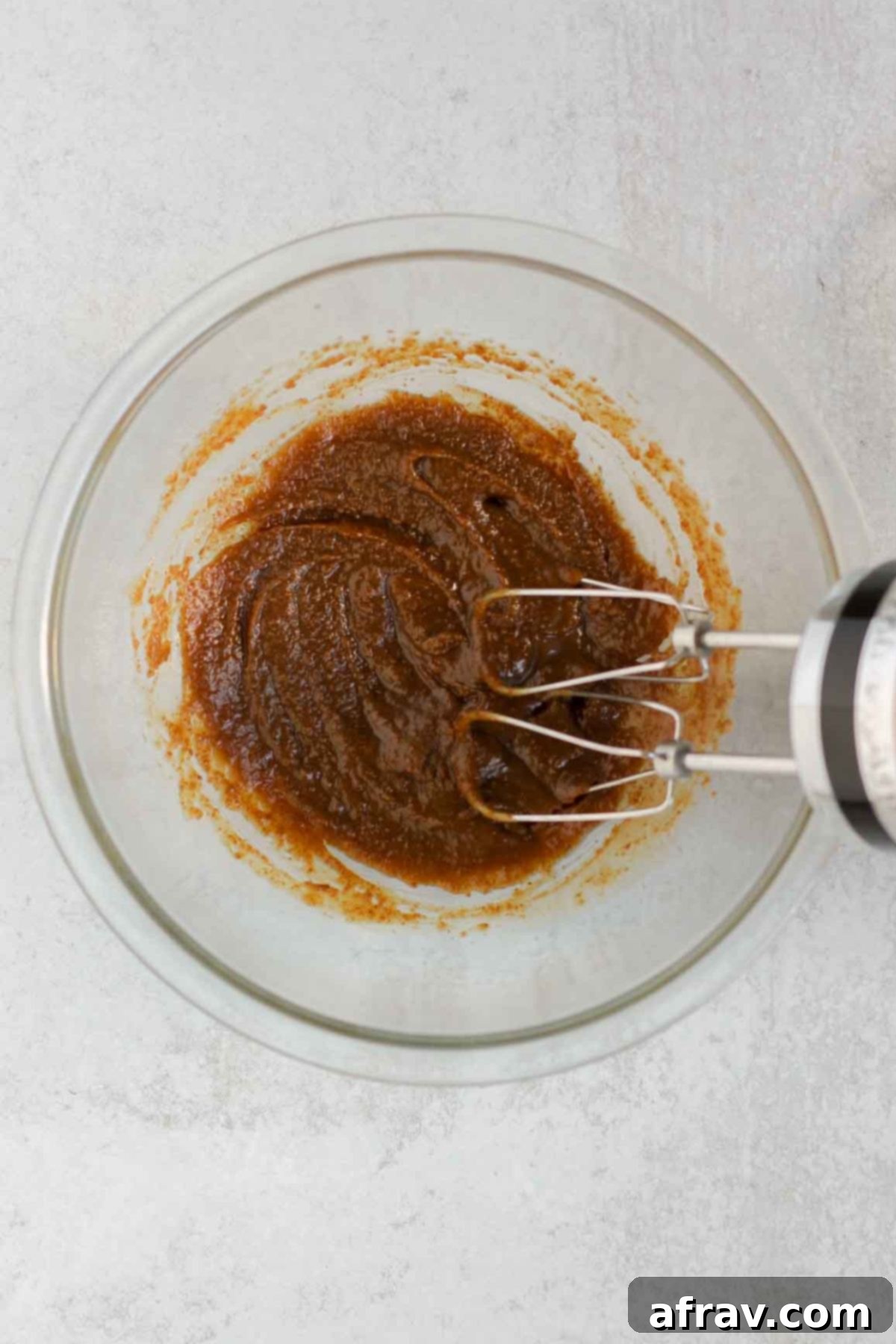 Melted butter and coconut sugar mixed together in a glass mixing bowl, forming a thick caramel-like mixture.