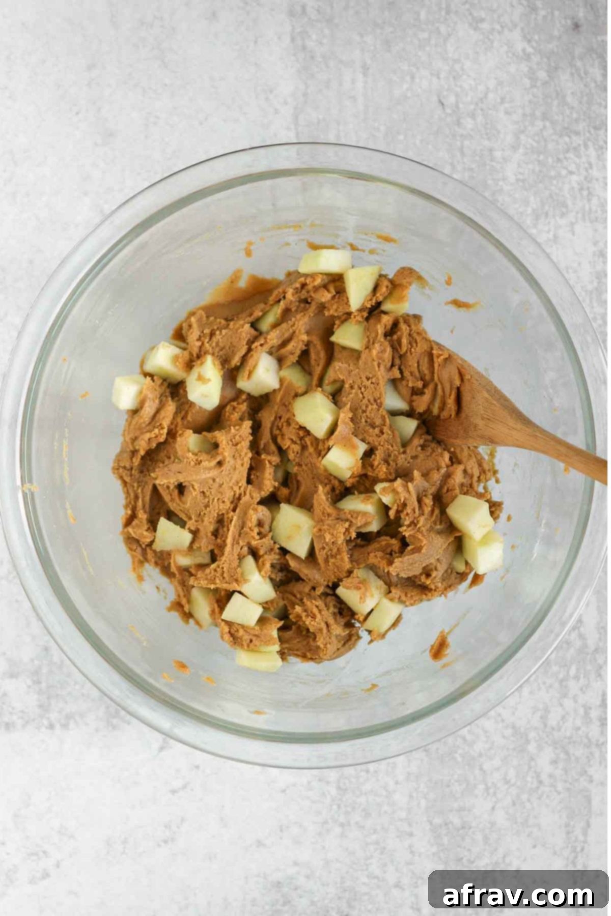 Gluten-free apple blondie batter in a glass mixing bowl with chopped apples folded in.