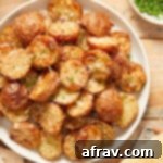 Overhead view of air fryer parmesan potatoes on a white plate next to chopped chives and parmesan cheese.