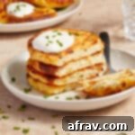 Stack of air fryer potato cakes on a plate with a dollop of sour cream and chopped chives on top.