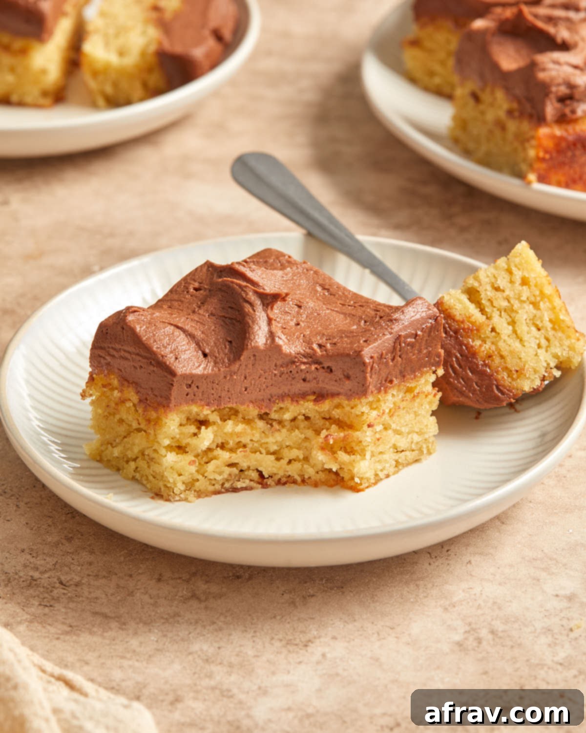 Side view of a slice of gluten-free almond flour banana cake with rich chocolate peanut butter frosting on a white plate, with a bite taken out, showcasing its moist texture.