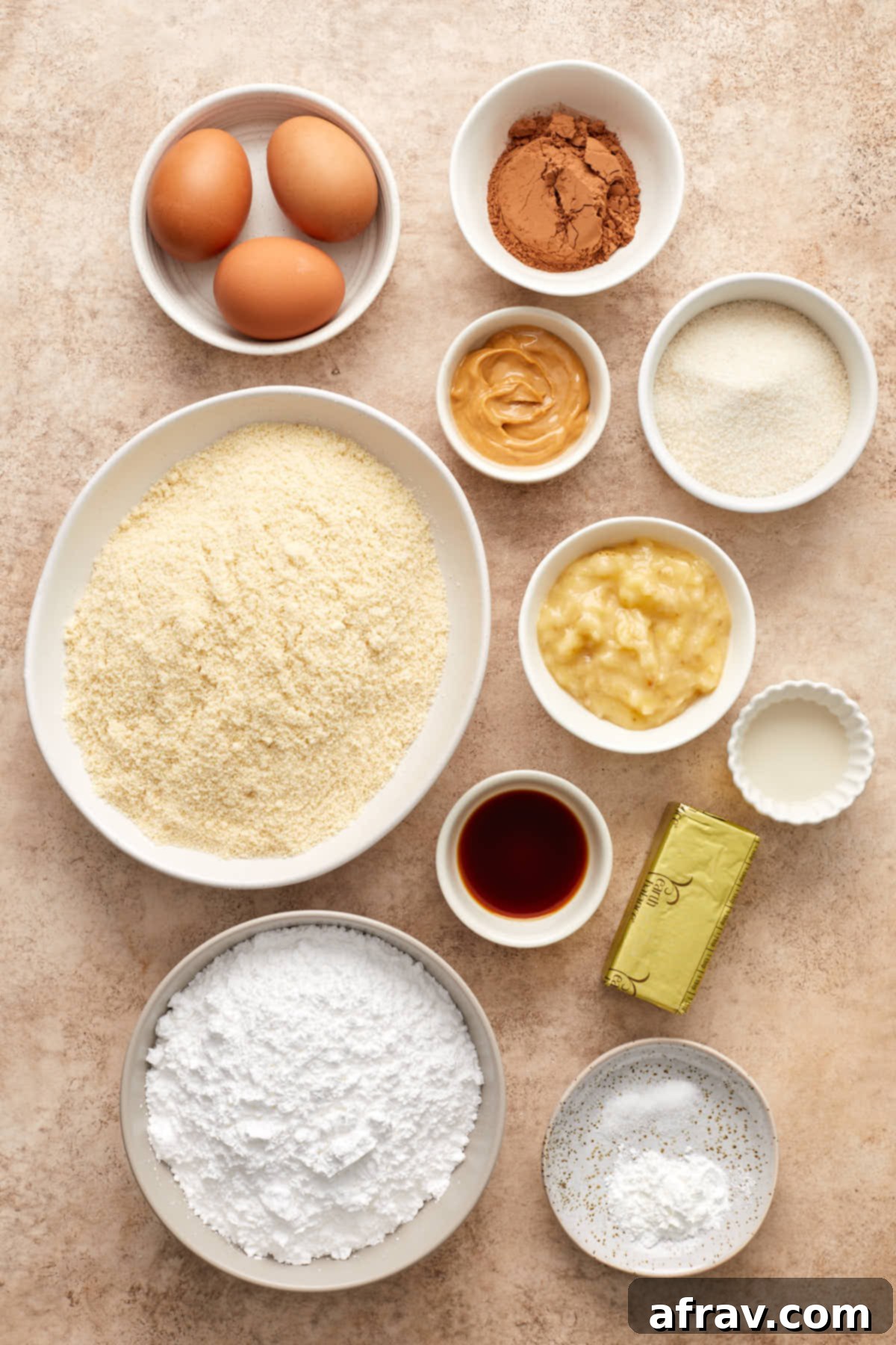 Individual bowls holding ingredients for almond flour banana cake, including blanched almond flour, baking powder, salt, eggs, mashed banana, cane sugar, vanilla extract, vegan butter, powdered sugar, cocoa powder, almond milk, and peanut butter.