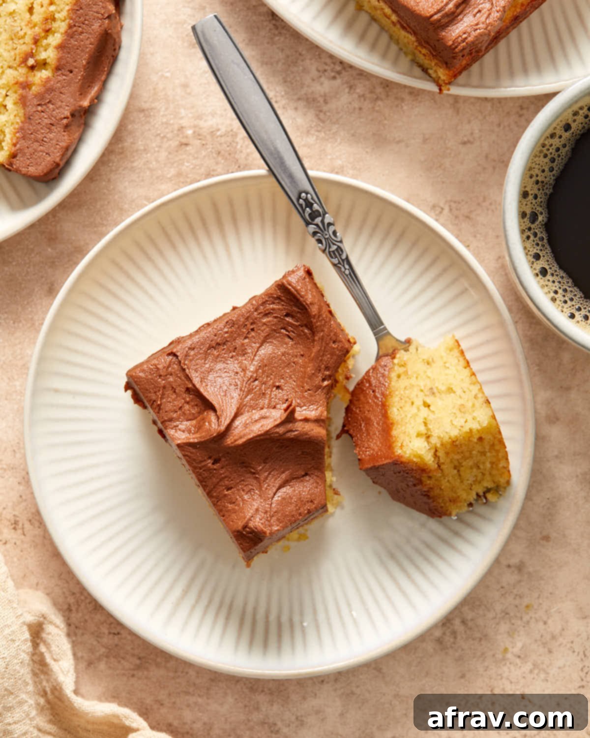 Overhead close-up view of a slice of almond flour banana cake with chocolate peanut butter frosting, with a fork gently removing a piece, highlighting the moist interior.