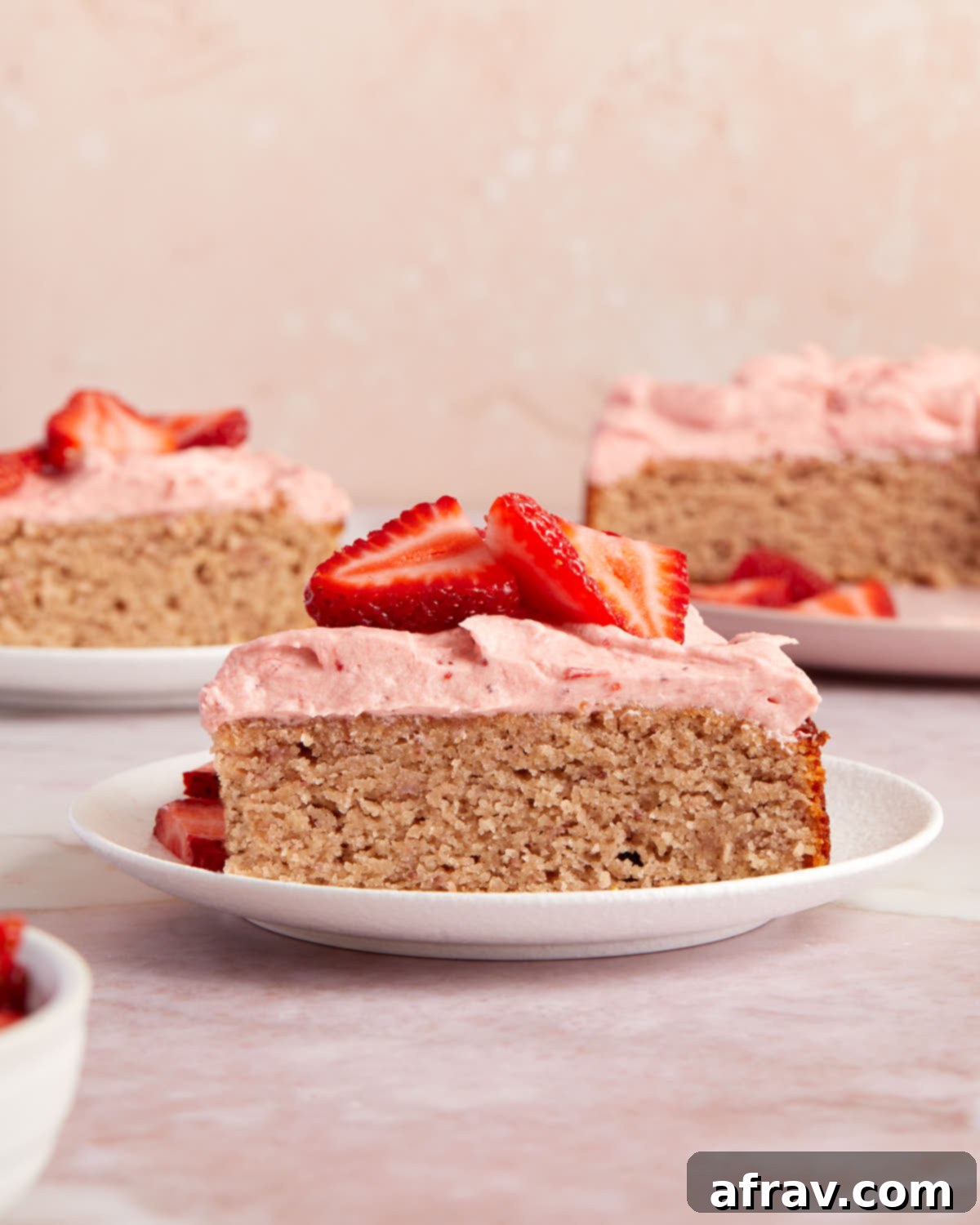 Side view of a slice of strawberry cake on a white plate and topped with fresh strawberries.