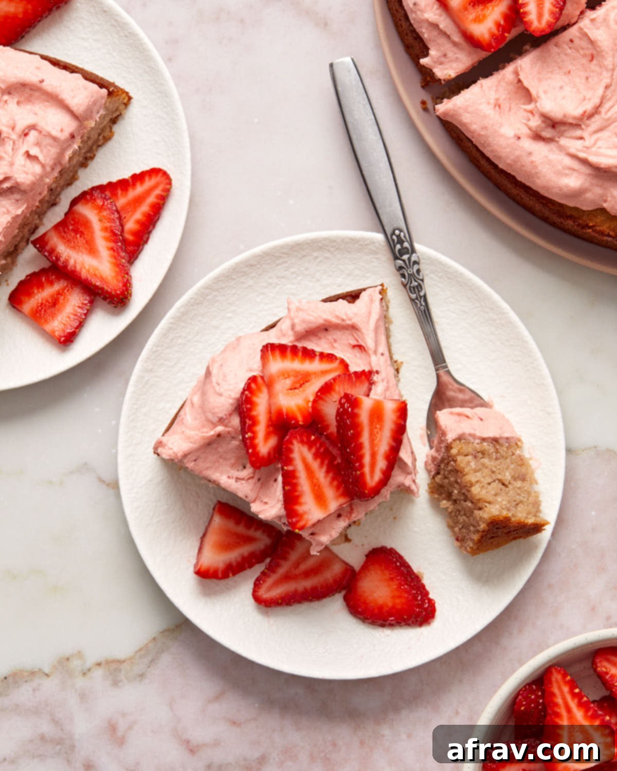 Overhead view of a slice of cake topped with strawberries and a fork removing a bite.