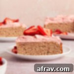 Side view of a slice of almond flour strawberry cake on a white plate with pieces of cake in the background.