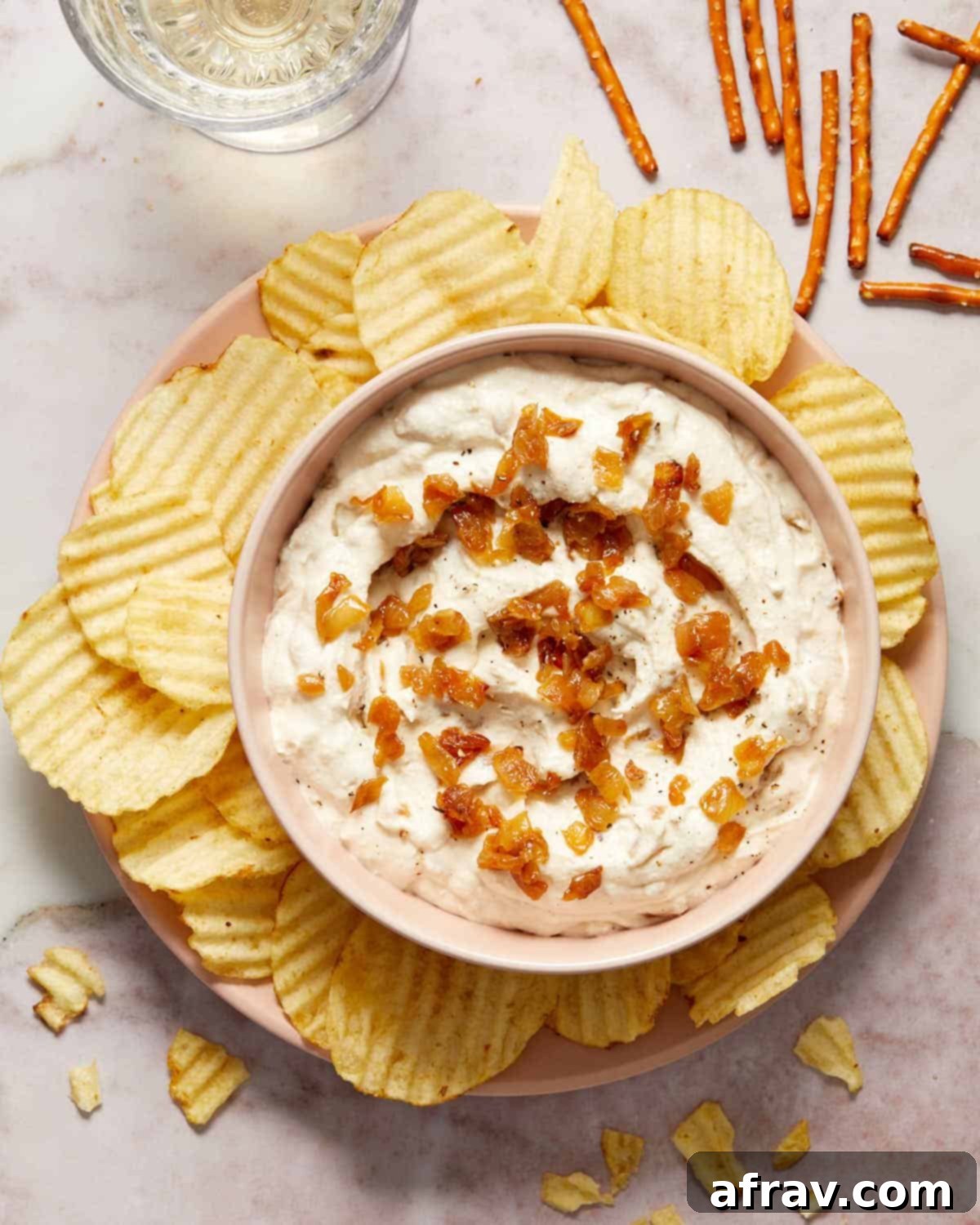 A bowl of creamy dairy-free caramelized onion dip topped with golden caramelized onions, surrounded by crispy potato chips, perfect for a party appetizer.