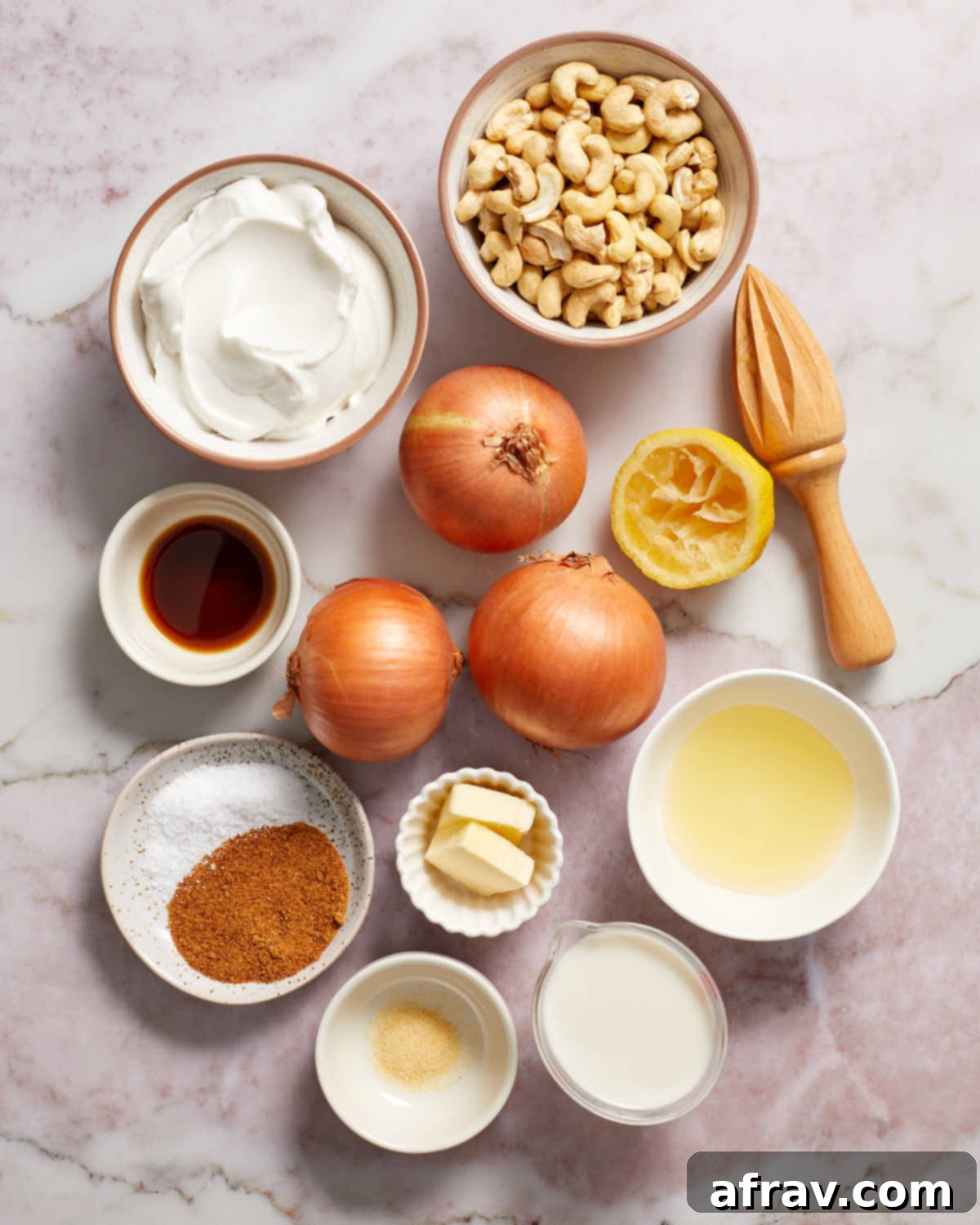 Array of fresh ingredients including three whole onions, a bowl of soaked cashews, dairy-free sour cream, and spices, all ready to make vegan caramelized onion dip.