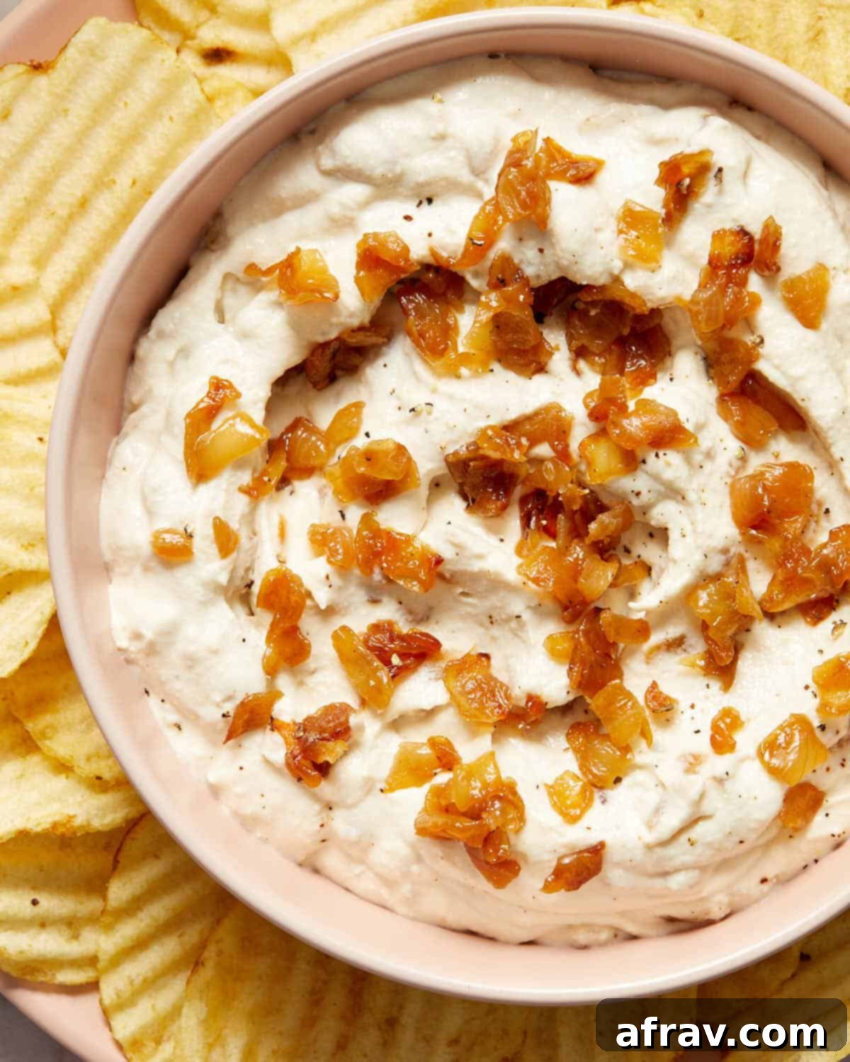 Close-up of the dairy-free caramelized onion dip in a rustic bowl, with a few potato chips casually placed on the side, highlighting its creamy texture.