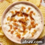 A top-down view of dairy-free caramelized onion dip in a white bowl, garnished with more onions, and surrounded by chips, a perfect vegan snack.