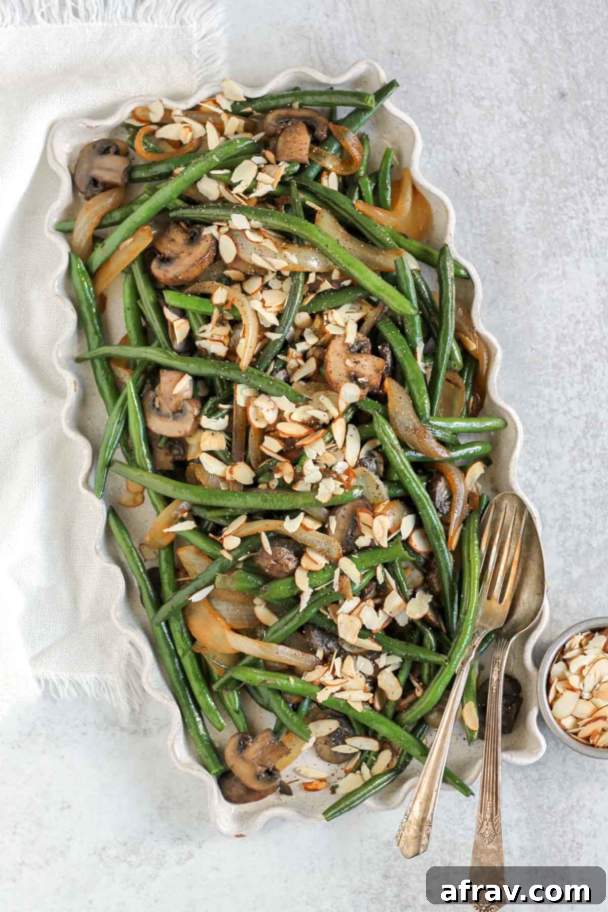 Savory Skillet Green Beans with Onions and Mushrooms 2 Green beans, onions, and mushrooms topped with sliced almonds on a rectangular serving platter.