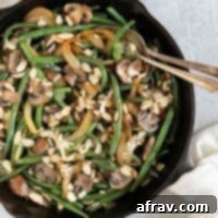 Savory Skillet Green Beans with Onions and Mushrooms 11 Green beans with mushrooms and onions topped with sliced almonds in a cast iron skillet with a vintage serving spoon and fork in the skillet.