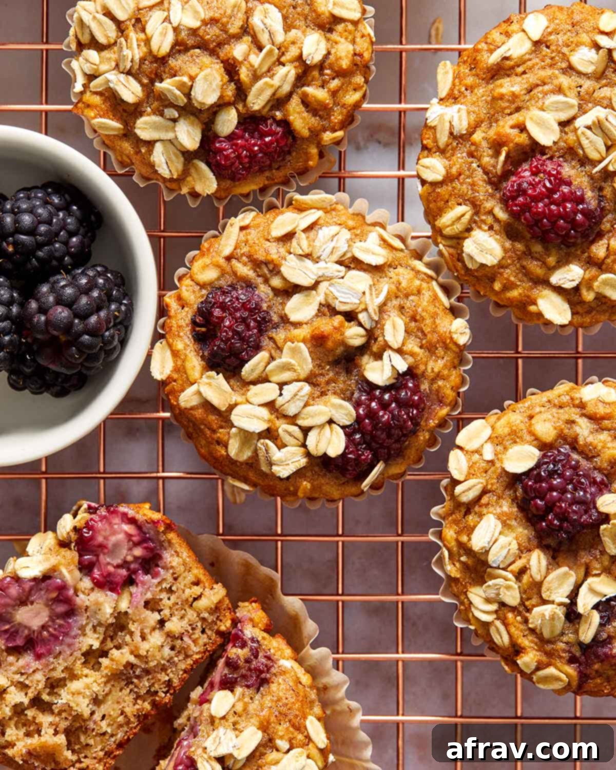 Overhead view of freshly baked banana blackberry oatmeal muffins cooling on a wire rack next to a small bowl of fresh blackberries.