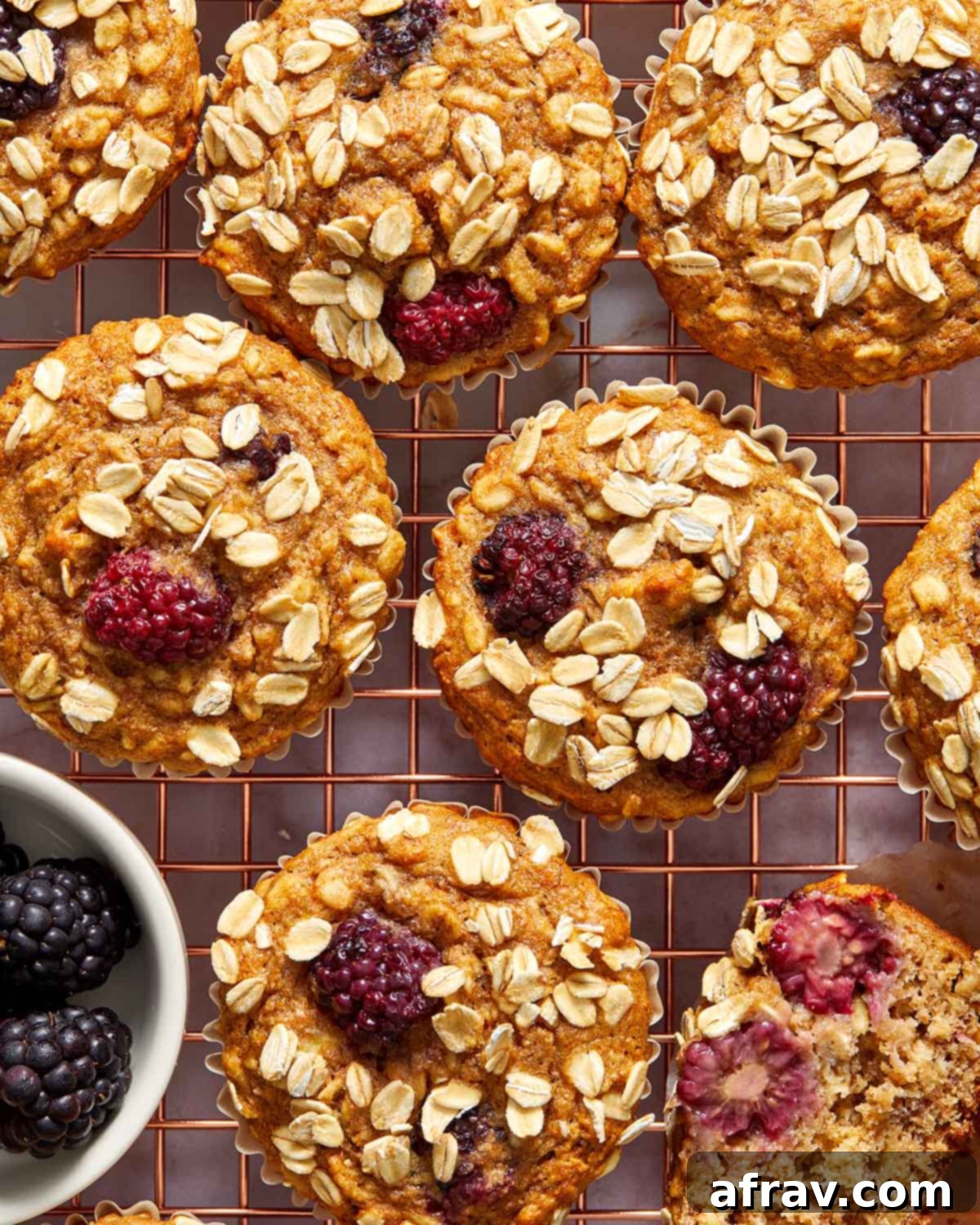 Close up view of several warm banana blackberry oatmeal muffins cooling on a gold coloured wire rack.