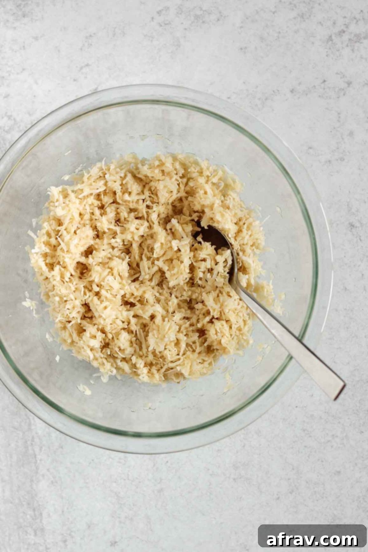 Shredded coconut mixed with egg whites and maple syrup in a medium glass mixing bowl.
