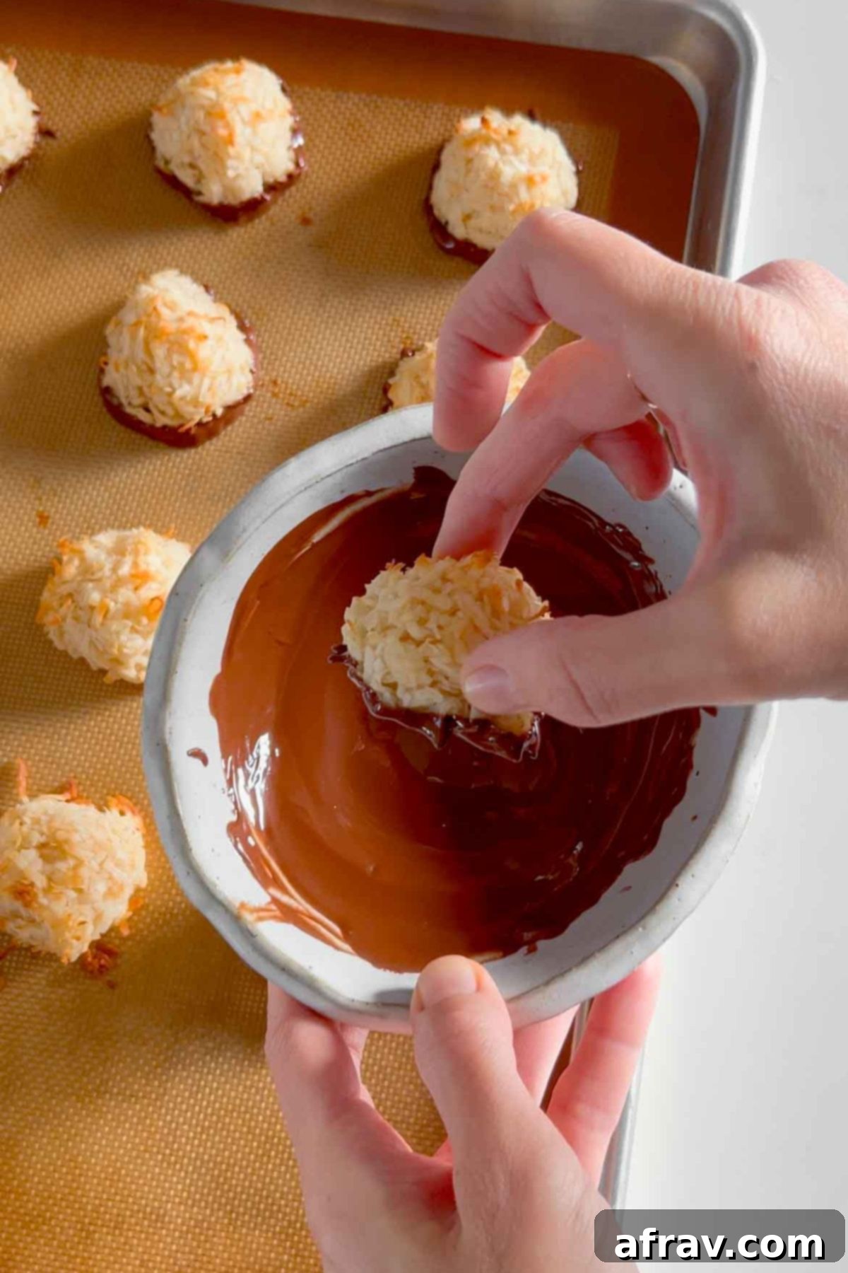 Hand dipping a single coconut macaroon cookie into a bowl of melted chocolate.