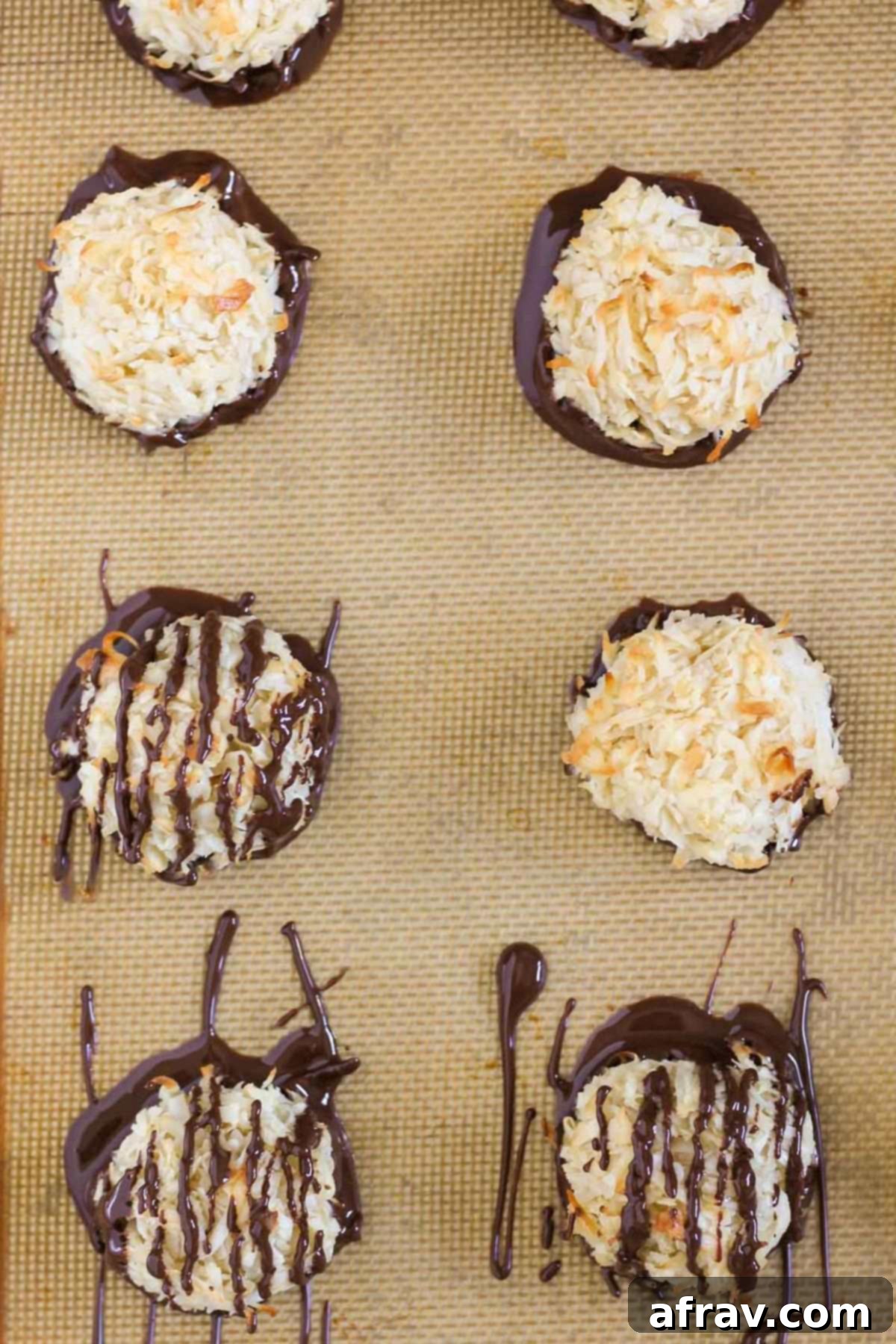 Coconut macaroon cookies that have been dipped in chocolate, some also drizzled with chocolate, on a baking sheet.