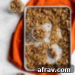 Pumpkin Spice Granola on a baking sheet with granola being spooned into glass jars.
