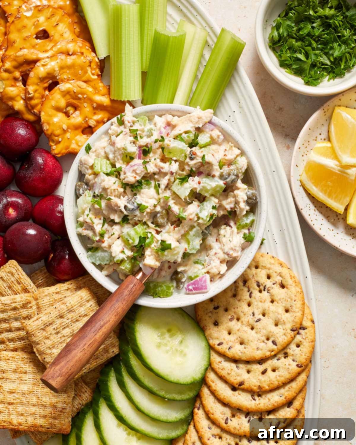 Overhead view of a vibrant bowl of no mayo tuna salad, surrounded by fresh veggies and an assortment of crackers.