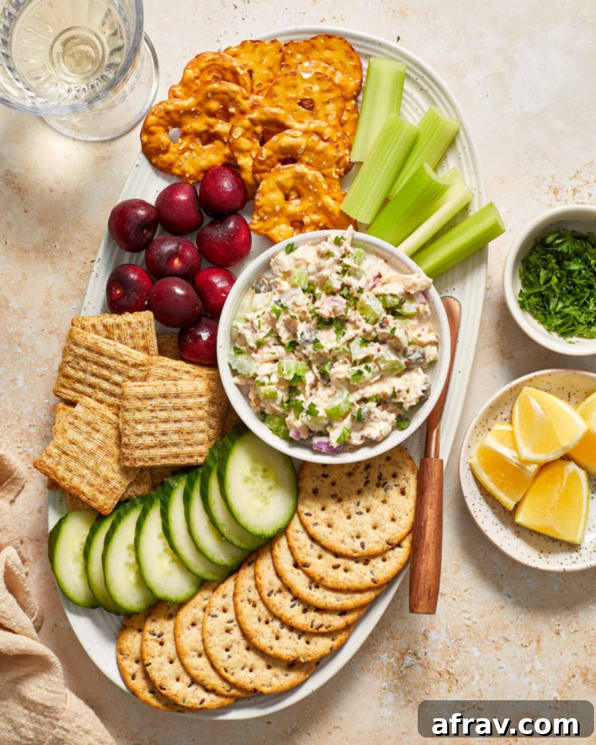 Beautifully presented tuna salad in a bowl, garnished with lemon wedges and chopped parsley, surrounded by crackers and fresh vegetables.