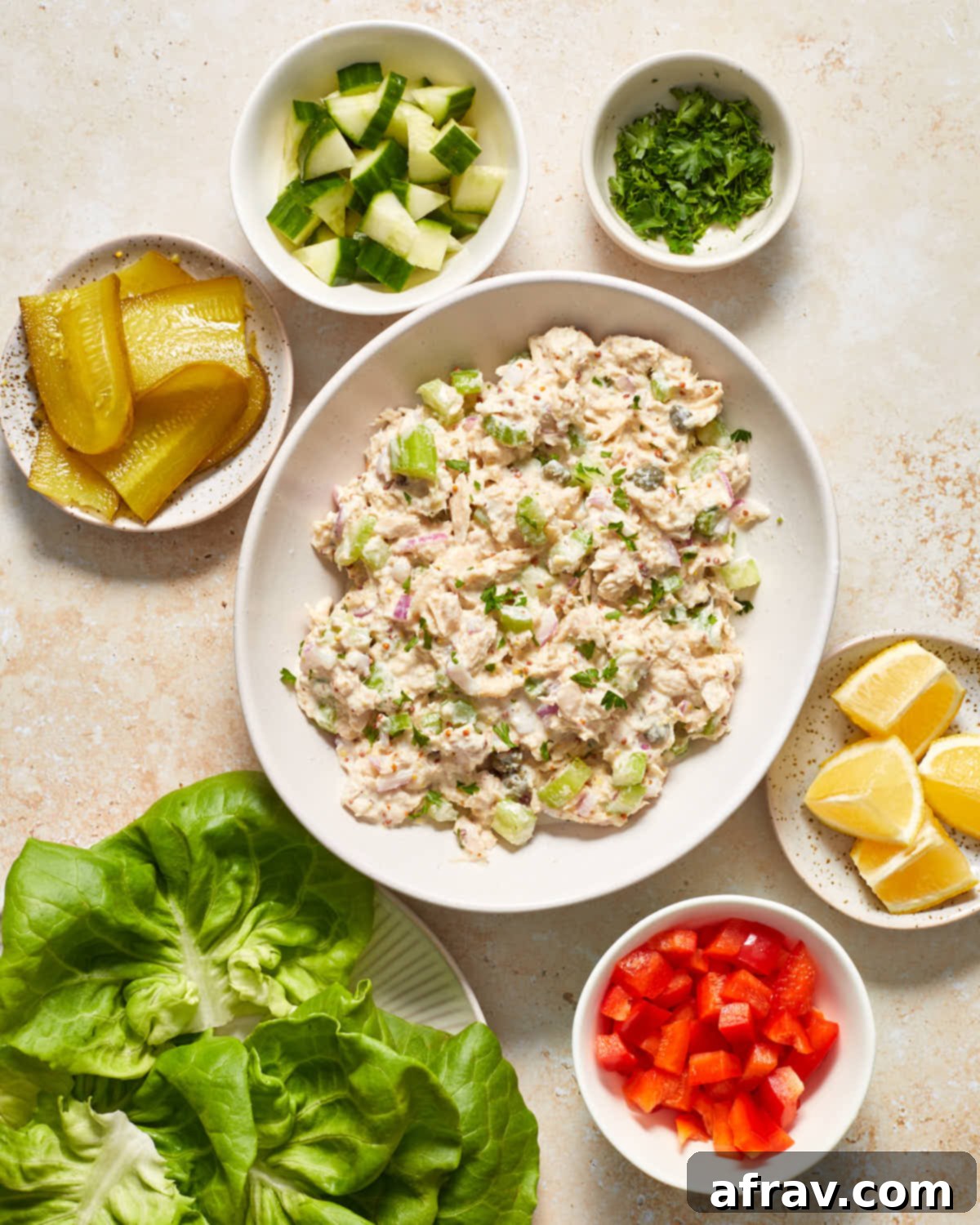 Individual ingredients neatly arranged on a white surface, showcasing tuna, fresh vegetables, pickles, and lettuce, ready to be combined for tuna lettuce wraps.