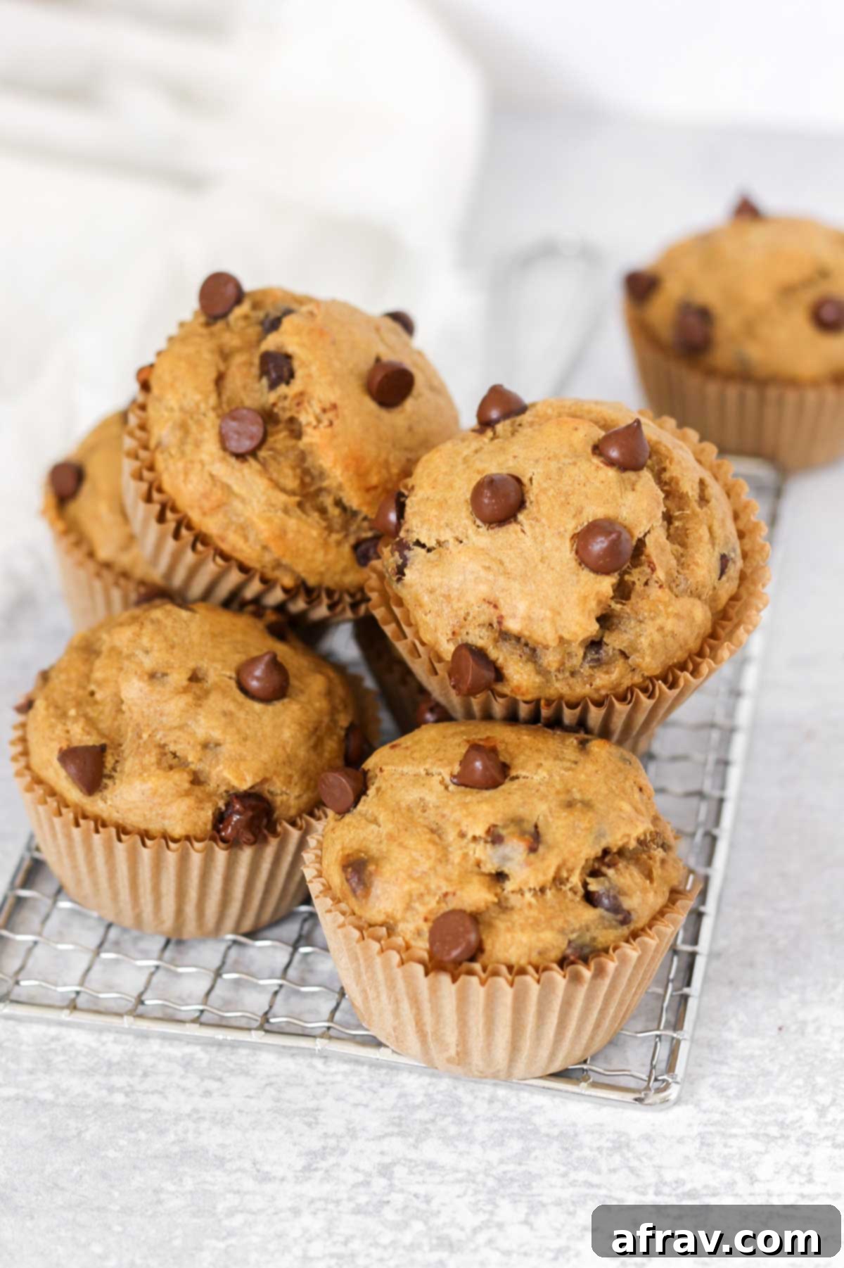 Stacked banana protein muffins with chocolate chips on a small rectangular wire cooling rack, highlighting their golden brown tops and melty chocolate.