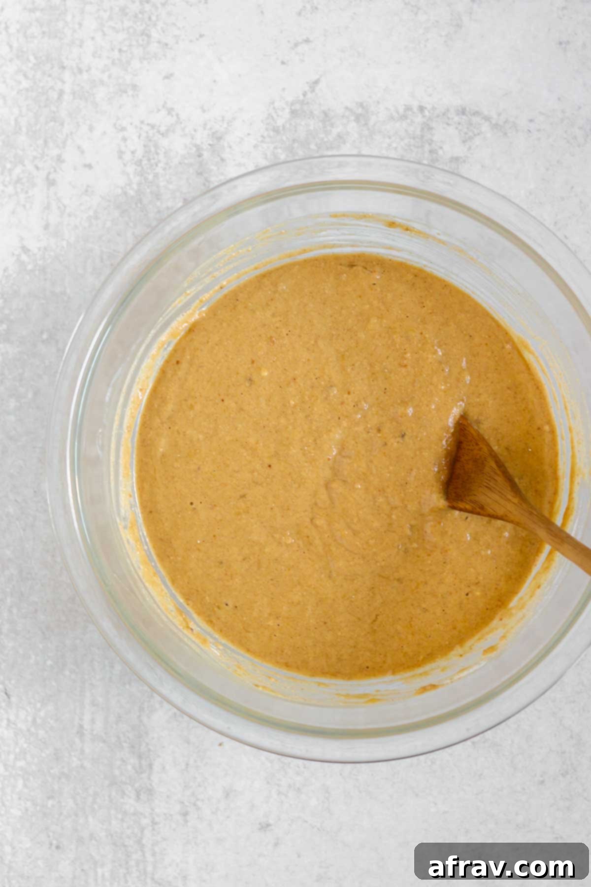 Banana protein muffin batter in a glass mixing bowl with a wooden spoon, showing the consistency before adding chocolate chips.