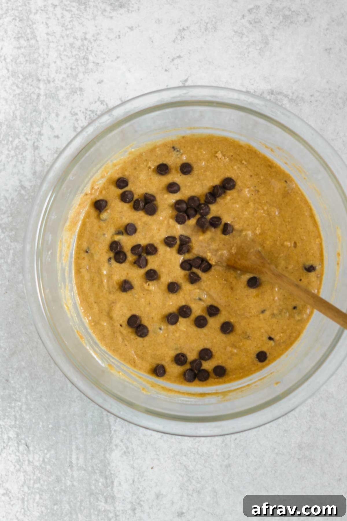 Banana protein muffin batter in a glass mixing bowl with chocolate chips mixed in the batter.